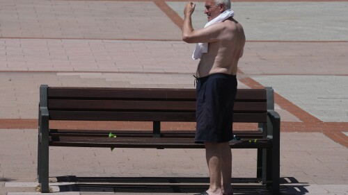 A man puts on his T-shirt in Madrid, Spain, Saturday, June 24, 2023. Temperatures in Madrid rose to around 35 degrees centigrade Saturday with hotter weather expected in the coming days. (AP Photo/Paul White)