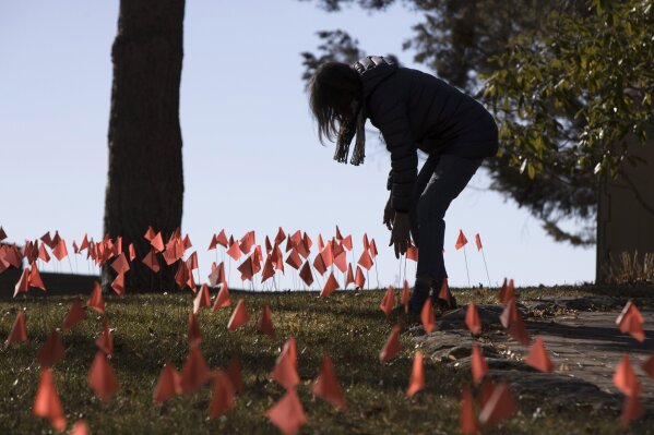 CORRECTS SPELLING OF LAST NAME ON FIRST REFERENCE - Cindy Pollock does maintenance on the construction flags in her front yard in Boise, Idaho, on Wednesday, Feb. 10, 2021. Pollock began planting the tiny flags across her yard — one for each of the more than 1,800 Idahoans killed by COVID-19 — the toll was mostly a number. Until two women she had never met rang her doorbell in tears, seeking a place to mourn the husband and father they had just lost. (AP Photo/Otto Kitsinger)