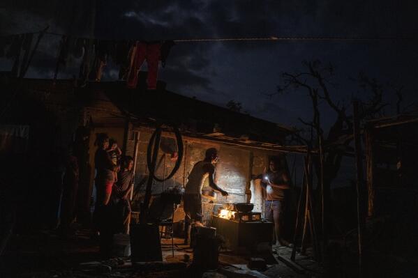 FILE - The Ramos family cooks dinner over a fire outside their storm-damaged home a week after Hurricane Ian knocked out electricity to the entire island, in La Coloma, Pinar del Rio province, Cuba, Oct. 5, 2022. Cuba's energy crisis has once again thrust the Caribbean island into the middle of an escalating tug-of-war between its seaside neighbor, the United States, and ally, Russia. Cuba sees the need to ease U.S. sanctions at the same time that it is benefitting from an influx of Russian oil. (AP Photo/Ramon Espinosa, File)