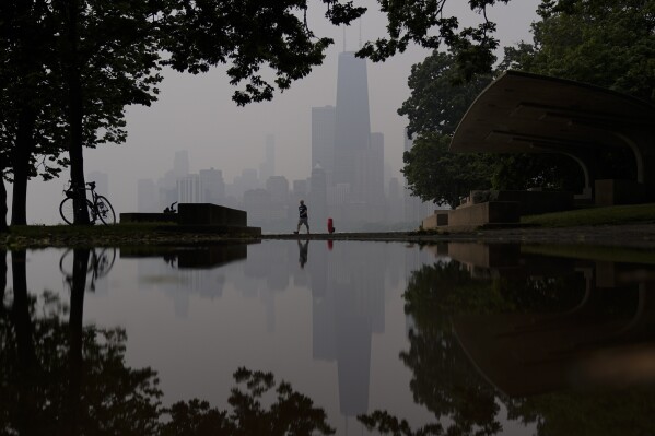 FILE - A person walks along the shore of Lake Michigan as the downtown skyline is blanketed in haze from Canadian wildfires, June 27, 2023, in Chicago. As smoky as the summer has been so far, scientists say it will likely be worse in future years because of climate change. (AP Photo/Kiichiro Sato, File)