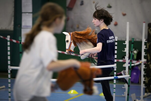A boy, right, and a girl attend a training session during a Hobby horsing competition in St. Petersburg, Russia, on Sunday, April 21, 2024. Several dozen kids, 48 girls and one boy, from first-graders to teenagers gathered in a gymnasium in northern St. Petersburg, Russia's second largest city, for a hobby horsing competition. (AP Photo/Dmitri Lovetsky)