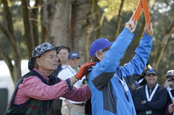 FILE - Bill Murray massages a volunteers shoulders on the fifth tee of the Monterey Peninsula County Club Shore Course during the second round of the AT&T Pebble Beach National Pro-Am golf tournament in Pebble Beach, Calif., in this Friday, Feb. 7, 2020, file photo.  The only stars at the AT&T Pebble Beach Pro-Am this year will be the players. The spike in COVID-19 cases in California led organizers to cancel the pro-am portion of a tournament. Pebble has a long history of entertainers and celebrities mixing with the pros on one of the most picturesque courses in the country. That means no antics from Bill Murray.(AP Photo/Tony Avelar, File)