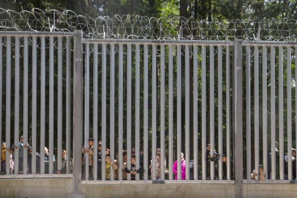 FILE - Members of a group of some 30 migrants seeking asylum look through the railings of a wall that Poland has built on its border with Belarus to stop massive migrant pressure, in Bialowieza, Poland, on Sunday, 28 May 2023. Poland’s main opposition leader has accused the conservative government of hypocrisy for allegedly admitting large numbers of foreign workers despite its anti-migrant rhetoric and a new border wall. (AP Photo/Agnieszka Sadowska, File)