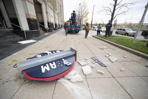 Workers from the Brilliant Electric Sign Company put out caution tape as pieces of the Cleveland Guardians team store sign lie on the ground in Cleveland, Friday, Nov. 19, 2021. The sign was being installed and fell off the building.  (AP Photo/Ken Blaze)