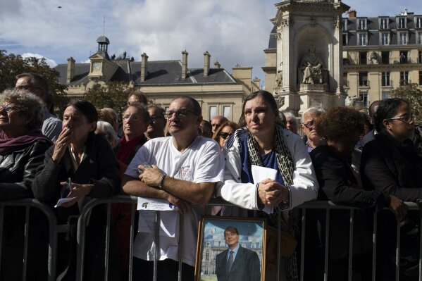 A mourner with a portrait of deceased former President Jacques Chirac watches the service on TV screens outside Saint Sulpice Church in Paris, Monday, Sept. 30, 2019, where past and current heads of states gathered to pay tribute to Chirac who died last week at the age of 86. (AP Photo/Rafael Yaghobzadeh)