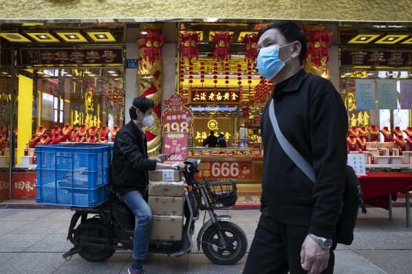 A walks past a delivery man outside a gold jewelry shop on the streets of Wuhan in central China's Hubei province on Wednesday, April 8, 2020. Streets in the city of 11 million people were clogged with traffic and long lines formed at the airport, train and bus stations as thousands streamed out of the city to return to homes and jobs elsewhere. (AP Photo/Ng Han Guan)