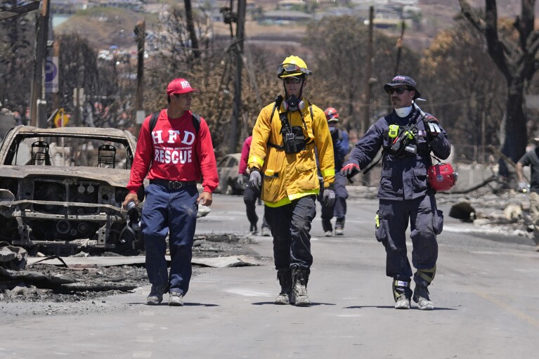 Miembros de un equipo de búsqueda y rescate caminan por una calle, el sábado 12 de agosto de 2023, en Lahaina, Hawái, luego de los extensos daños causados ​​por incendios forestales.  (Foto AP/Rick Bomer)