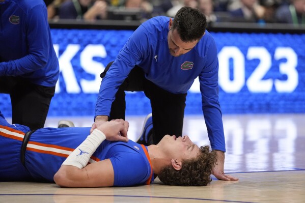 Florida head coach Todd Golden kneels nexrt to center Micah Handlogten (3) after he injured his leg during the first half of an NCAA college basketball game against Auburn at the Southeastern Conference tournament Sunday, March 17, 2024, in Nashville, Tenn. Handlogten was taken off teh court on a stretcher. (AP Photo/John Bazemore)