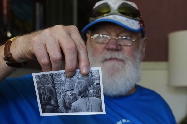Dean Kahler, who was shot an paralyzed at Kent State University on May 4, 1970, holds a photograph he took of a U.S. National Guardsman talking to students during the 1970 anti-war protest, during an interview in his home Thursday, May 2, 2024, in Plain Township, Ohio. (AP Photo/Sue Ogrocki)