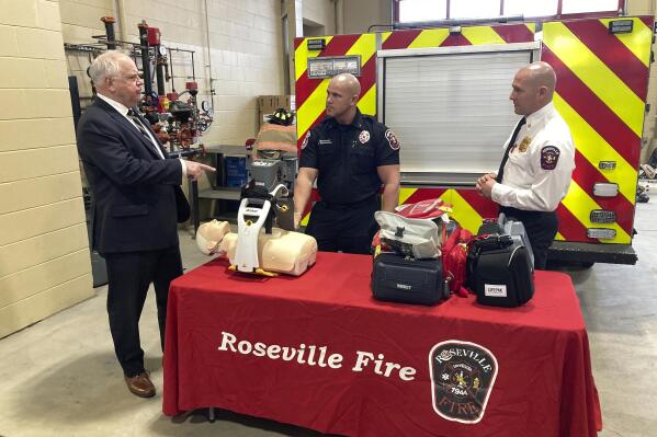 Minnesota Gov. Tim Walz, left, watches a demonstration at the Roseville, Minn., Fire Department Monday, Jan. 23, 2023, of a machine that performs chest compressions to help first responders perform CPR. Discussing the LUCAS device with him are Lt. Cody Thornberg, center, and Fire Chief David Brosnahan, right. Walz went to the station in suburban St. Paul, to roll out more pieces of his budget, including $300 million to support public safety agencies across the state. (AP Photo/Steve Karnowski)