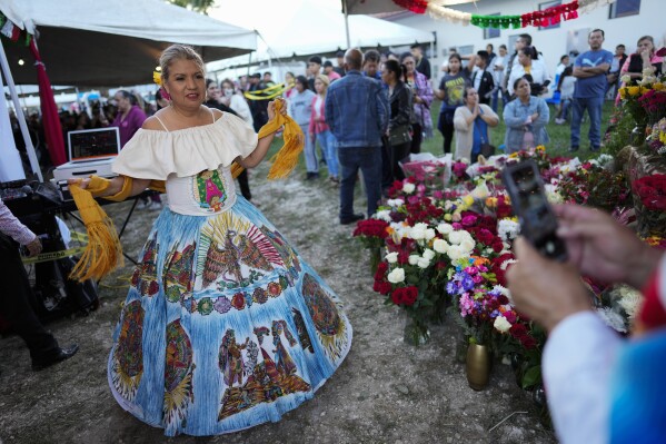A festival goer takes a picture of Margarita Garza, 61, as she wears a skirt featuring Aztec designs and a shirt with an embroidered image of the Virgin of Guadalupe, one of several apparitions of the Virgin Mary witnessed by an indigenous Mexican man named Juan Diego in 1531, at St. Ann Mission in Naranja, Fla., Sunday, Dec. 10, 2023. Garza immigrated to the US from Mexico in 1977. For this mission church where Miami's urban sprawl fades into farmland and the Everglades swampy wilderness, it's the most important event of the year, both culturally and to fundraise to continue to minister to the migrant farmworkers it was founded to serve in 1961. (AP Photo/Rebecca Blackwell)