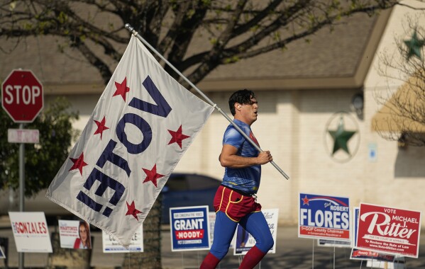 Dressed as Superman and holding a "Vote!" flag, Artist David Alcantar jogs past a polling site, Tuesday, March 5, 2024, in San Antonio. The flag and costume are part of an art project to encourage voting. (AP Photo/Eric Gay)