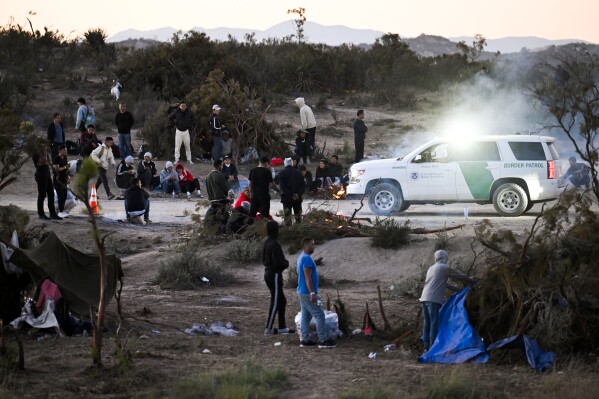 A U.S. Border Patrol agent in a vehicle watches a group of asylum-seekers at a camp after they crossed the nearby border with Mexico, Tuesday Sept. 26, 2023, near Jacumba Hot Springs, Calif. Migrants continue to arrive to desert campsites along California's border with Mexico, as they await processing. (AP Photo/Denis Poroy)