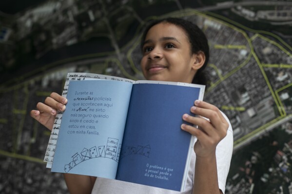 Myrella Victoria Viana dos Santos, 10, shows the book titled “I was supposed to be at school” that includes her experiences of living in the Mare favela of Rio de Janeiro, Brazil, Monday, March 25, 2024. Dozens of kids and teenagers from one of Rio de Janeiro's most violent favelas gathered on Monday to celebrate their most important piece of work yet: a book that aims to show authorities how they see police violence in their Maré community from a young age. (AP Photo/Bruna Prado)