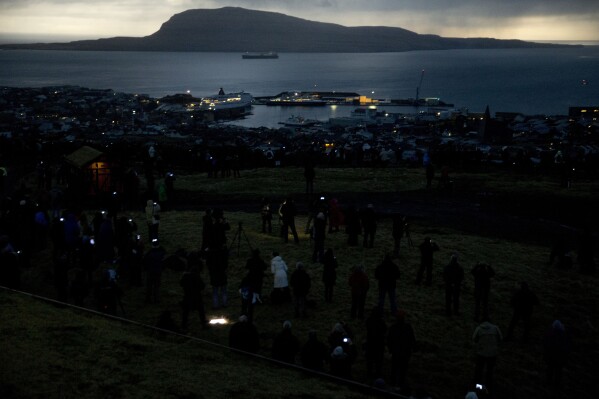 FILE - People watch in darkness during the totality of a solar eclipse on as seen from a hill beside a hotel on the edge of the city overlooking Torshavn, the capital city of the Faeroe Islands, Friday, March 20, 2015. (AP Photo/Matt Dunham, File)