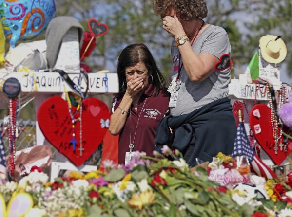 FILE - Marjory Stoneman Douglas High School administrative employees Margarita LaSalle, left, and JoEllen Berman, walk along the hill near the school lined with 17 crosses to honor the students and teachers killed on Valentine's Day, as teachers and staff returned to the school, Feb. 23, 2018, in Parkland, Fla. There have been dozens of shootings and other attacks in U.S. schools and colleges over the years, but until the massacre at Colorado's Columbine High School in 1999, the number of dead tended to be in the single digits. Since then, the number of shootings that included schools and killed 10 or more people has mounted. (Charles Trainor Jr/Miami Herald via AP, File)