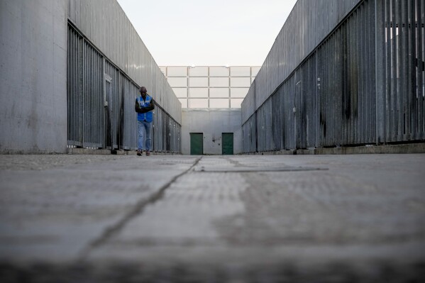 A volunteer walks in an open area of the Ponte Galeria center, one of the facilities created in Italy to detain migrants ahead of their repatriation, as they are considered ineligible for refugee status or international protection, in Rome, Italy, Tuesday, March 19, 2024. (AP Photo/Andrew Medichini)