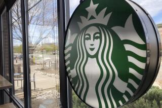A sign bearing the corporate logo hangs in the window of a Starbucks open only to take-away customers in this photograph taken Monday, April 26, 2021, in southeast Denver.  Starbucks is no longer requiring its U.S. workers to be vaccinated against COVID-19, reversing a policy it announced earlier this month. The Seattle coffee giant says, Wednesday, Jan. 19, 2022,  it's responding to last week’s ruling by the U.S. Supreme Court.  (AP Photo/David Zalubowski)