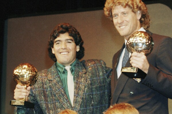 ARCHIVO - La estrella argentina Diego Maradona, izquierda, y el portero de Alemania Occidental Harald Schumacher sostienen sus trofeos de la Copa Mundial de Fútbol mientras posan con dos jóvenes futbolistas durante la ceremonia del Premio de la Bota de Oro de Fútbol celebrada en París, Francia, el 13 de noviembre de 1986. Los herederos de Diego Maradona presentaron una demanda para tratar de detener la subasta de un trofeo que le fue otorgado tras el Mundial de 1986 ganado por Argentina. (Foto AP/Michael Lipchitz, archivo)