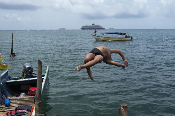 A youth dives into the sea from Gardi Sugdub Island, part of the San Blas archipelago off Panama's Caribbean coast, Sunday, May 26, 2024. Due to rising sea levels, about 300 Guna Indigenous families will relocate to new homes, built by the government, on the mainland. (AP Photo/Matias Delacroix)