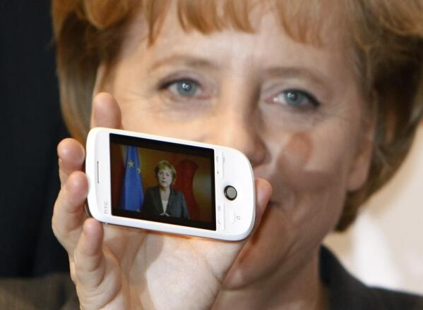 FILE - In this Tuesday, March 3, 2009 file photo German Chancellor Angela Merkel holds a cell phone with a photo of her on the screen during her opening walk at the CeBIT in Hanover, northern Germany. Cybersecurity researchers in Europe say they've discovered a flaw in an encryption algorithm used by cellphones that may have allowed attackers to eavesdrop on some data traffic for more than two decades. In a paper published Wednesday, researchers from Germany, France and Norway said the flaw affects the GPRS mobile data standard. (AP Photo/Joerg Sarbach, file)