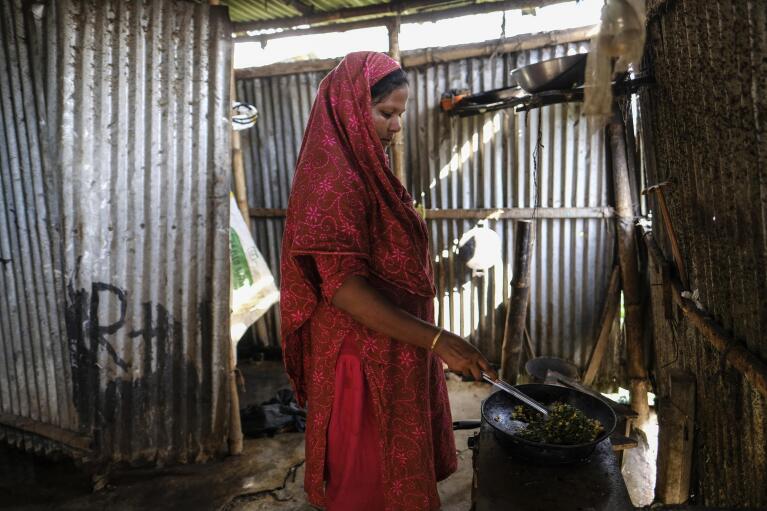 Arzu Begum prepares a meal inside a kitchen in the poor Mirpur area of Dhaka, Bangladesh on July 3, 2022. Mohammad Jewel and Begum were forced to flee Ramdaspur village in Bangladesh last year when the Meghna River flooded and destroyed their home. The couple and their four sons moved to the capital, Dhaka, where they struggle to pay their rent and food bills on their small incomes. (AP Photo/Mahmud Hossain Opu)