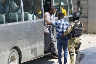 FILE - Former coup leader Guy Philippe, wearing a gray sweatsuit, descends from a bus at Haiti's National Police station, in Port-au-Prince, Nov. 30, 2023, after he was repatriated from the U.S. Supporters of Philippe launched protests on Monday, Jan. 15, 2024, that have paralyzed some cities across Haiti as they demand the resignation of Prime Minister Ariel Henry. (AP Photo/Odelyn Joseph, File)