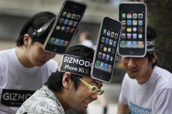 FILE - iPhone fans share a light moment while waiting for the first day sales of iPhone 3GS in Tokyo, Japan, Friday, June 26, 2009. Longtime technology news and review site Gizmodo has been sold for the third time in the past eight years. (AP Photo/Junji Kurokawa, File)