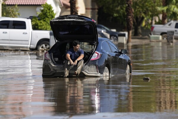 Dorian Padilla sits in his car as he waits for a tow after it got stuck in the mud on a street Monday, Aug. 21, 2023, in Cathedral City, Calif. Forecasters said Tropical Storm Hilary was the first tropical storm to hit Southern California in 84 years, bringing the potential for flash floods, mudslides, isolated tornadoes, high winds and power outages. (AP Photo/Mark J. Terrill)