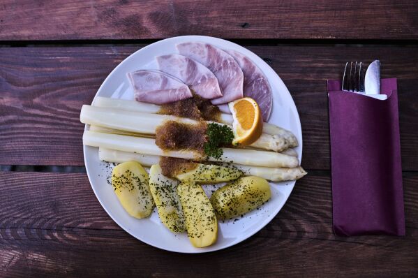 A plate with fresh white asparagus, ham, potatoes and melted butter is served at the Jakobs-Hof farm asparagus restaurant in Beelitz Germany, Thursday, April 3, 2025. (AP Photo/Markus Schreiber)