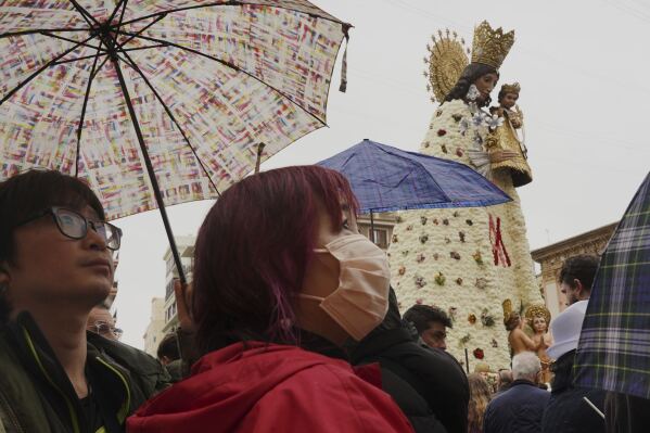 Tourists look at a figure of the Virgin decorated with a floral mantle, in honor of those who died during the past floods, during the Fallas festival in Valencia, Spain, on Wednesday, March 19, 2025. (AP Photo/Alberto Saiz)
