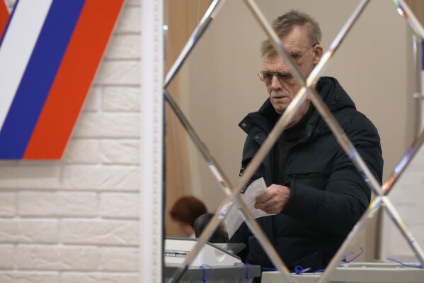 A man is reflected in a mirror as he casts a ballot at a polling station during the presidential elections in St. Petersburg, Russia, Saturday, March 16, 2024. Voters in Russia headed to the polls for a presidential election that was all but certain to extend President Vladimir Putin's rule after he clamped down on dissent. (AP Photo/Dmitri Lovetsky)