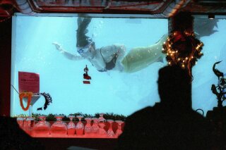 This 2012 file photo shows a woman dressed as a mermaid swimming in the pool through a window of the Sip N' Dip Lounge in Great Falls, Mont. The mermaids were scheduled to go back to work on Wednesday, May 6, 2020, after the Montana governor's office clarified that hotel pools are included in his directive to ease coronavirus restrictions. (Larry Beckner/Great Falls Tribune via AP, File)