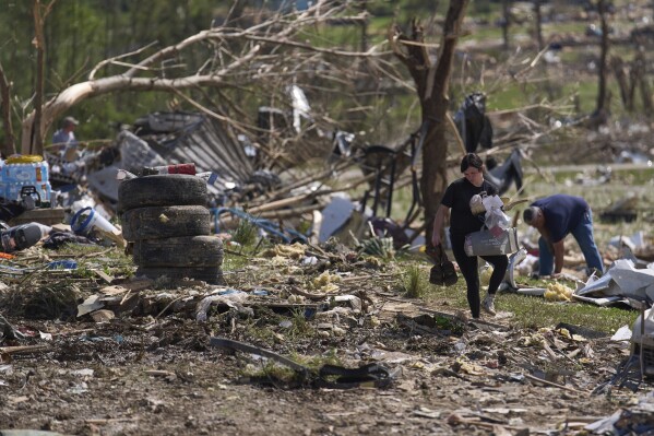 Macy Coffey carries salvaged items from Edwina Wilson's destroyed home on Sunday, May 18, 2025, in London, Kentucky. (AP Photo/Caroline Custer)