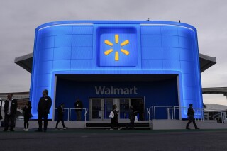 FILE - People walk by the Walmart booth during the CES tech show Tuesday, Jan. 9, 2024, in Las Vegas. Walmart is offering new perks for its hourly workers. They include a new bonus plan as well as opportunities to move into skilled trade jobs within the company. (AP Photo/John Locher, file)