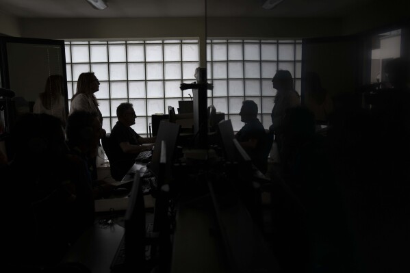 Head of Anti Mafia force (DIA), Carla Durante, left, is silhouetted has she talks with her team in the wire-tape room of the DIA headquarters in Lecce, Italy, Tuesday, May 21, 2024. (AP Photo/Alessandra Tarantino)