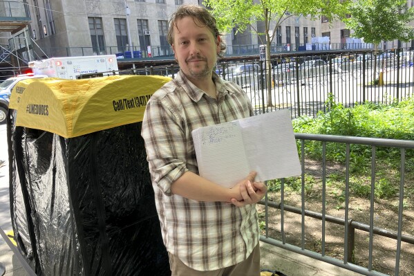 Richard Partington poses for a photo while holding up a line list outside Manhattan Criminal Court, Friday, May 24, 2024, in New York. The word has gotten out that members of the public can attend former President Donald Trump's trial in New York City and the line to get inside the courtroom has gotten longer. A handful of people, including 43-year-old Partington of East Hampton, N.Y., were already lined up Friday for the chance to witness closing arguments on Tuesday. (AP Photo/Karen Matthews)