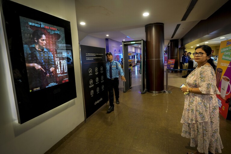 A woman stands in front of a poster of the movie Article 370 displayed at a cinema hall in Guwahati, India, Thursday, March 21, 2024. The movie is one of several upcoming Bollywood releases based on polarizing issues, which either promote Indian Prime Minister Narendra Modi and his government’s political agenda, or lambast his critics. (AP Photo/Anupam Nath)