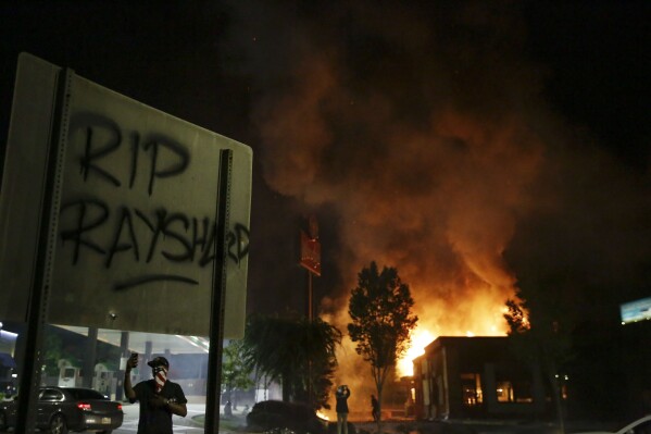 FILE- In this June 13, 2020 file photo, "RIP Rayshard" is spray-painted on a sign as flames engulf a Wendy's restaurant where Rayshard Brooks was shot and killed by police in Atlanta. Two of three people charged with arson in the burning of the restaurant have pleaded guilty after reaching deals with prosecutors. (AP Photo/Brynn Anderson, File)
