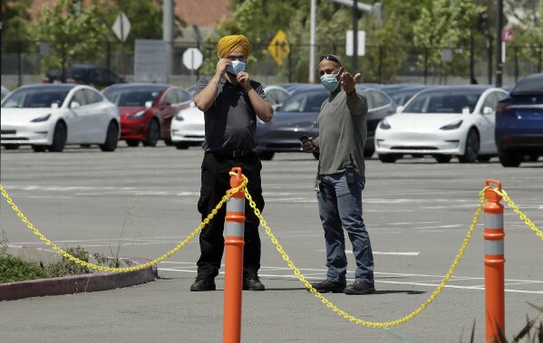 Men don masks as they guard new Tesla vehicles at the Tesla plant Monday, May 11, 2020, in Fremont, Calif. The parking lot was nearly full at Tesla's California electric car factory Monday, an indication that the company could be resuming production in defiance of an order from county health authorities. (AP Photo/Ben Margot)
