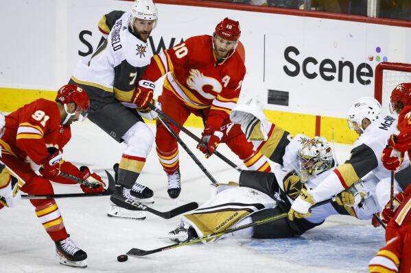 Vegas Golden Knights goalie Logan Thompson scrambles to block the net as Calgary Flames forward Nazem Kadri, left, and forward Jonathan Huberdeau, third left, chase the puck while Knights defenseman Alex Pietrangelo, second from left, watches during the second period of an NHL hockey game Tuesday, Oct. 18, 2022, in Calgary, Alberta. (Jeff McIntosh/The Canadian Press via AP)