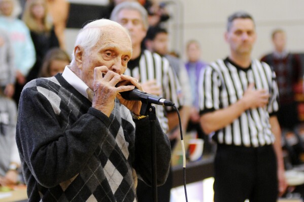 FILE - Former Brooklyn Dodgers baseball player Carl Erskine plays the national anthem on his harmonica before a college basketball game between Anderson and Franlin in Anderson, Ind., Saturday, Jan. 14, 2017. Carl Erskine, who pitched two no-hitters as a mainstay on the Brooklyn Dodgers and was a 20-game winner in 1953 when he struck out a then-record 14 in the World Series, died Tuesday, April 16, 2024, at Community Hospital Anderson in Anderson, Ind., according to Michele Hockwalt, the hospital’s marketing and communication manager. He was 97. (Don Knight/The Herald-Bulletin via AP, File)