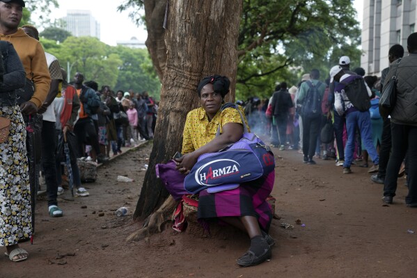 A woman takes a break from the queue outside the passport offices in Harare, Wednesday, Dec. 20, 2023. Atop many Christmas wish lists in economically troubled Zimbabwe is a travel document and people are flooding the passport office this holiday season ahead of a price hike planned in the New Year. The desperation at the office in the capital is palpable as some people fear the hike could push the cost of obtaining a passport out of reach and economic gloom feeds a surge in migration. (AP Photo/Tsvangirayi Mukwazhi)