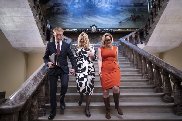 Sen. James Lankford, R-Okla., left, the lead GOP negotiator on a border-foreign aid package, holds hands with his wife Cindy Lankford, center, joined at right by Sen. Kyrsten Sinema, I-Ariz., who has been central to Senate border security talks, during procedural votes, at the Capitol in Washington, Wednesday, Feb. 7, 2024. Senate Republicans have blocked the bipartisan border package, scuttling months of negotiations between the two parties on legislation intended to cut down record numbers of illegal border crossings. (APPhoto/J. Scott Applewhite)