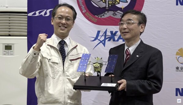 In this image made from video provided by JAXA, its project manager Yuichi Tsuda, left, and Hitoshi Kuninaka, Director General of ISAS/JAXA, pose with a Hayabusa2 model, during a press conference i...