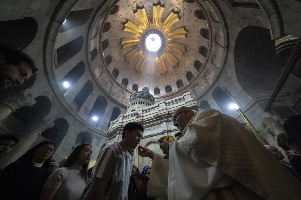 A priest offers a communion wafer to a faithful during the Easter Sunday Mass led by the Latin Patriarch at the Church of the Holy Sepulchre, where many Christians believe Jesus was crucified, buried and rose from the dead,, in the Old City of Jerusalem, Sunday, March 31, 2024. (AP Photo/Leo Correa)