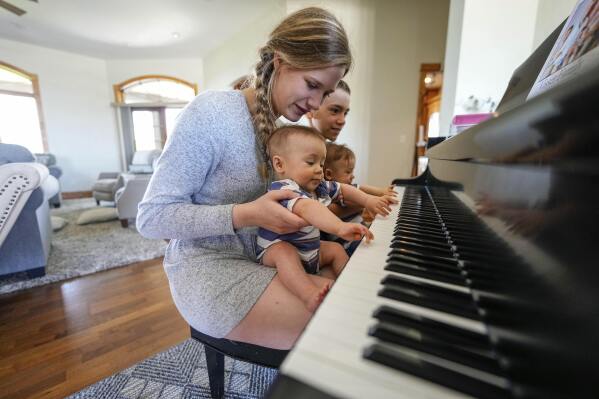 Fourteen-year-old Abby Visser and eleven-year-old William Visser hold their embryo-adopted six-month-old brothers Collin and Jackson at the piano in their home, Monday, May 13, 2024, in Sterling, Colorado. When faced with infertility, Christians who believe life begins at or around conception wrestle with the ethics of IVF and how to build a family in a way that conforms with their beliefs. (AP Photo/Jack Dempsey)
