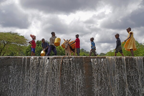 Crianças enchem latas com água de uma barragem de areia no condado de Makueni, Quénia, na sexta-feira, 1 de março de 2024. A construção de barragens de areia, uma estrutura para recolher água de rios sazonais, ajuda a minimizar a perda de água por evaporação e recarrega as águas subterrâneas. (Foto AP/Brian Inganga)