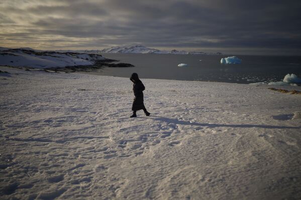 A woman walks along the shore of a beach while pieces of ice float in the sea of Nuuk, Greenland, Friday, Feb. 14, 2025. (AP Photo/Emilio Morenatti)