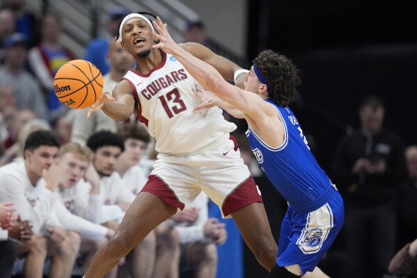 Washington State's Isaac Jones (13) passes around Drake's Conor Enright during the second half of a first-round college basketball game in the NCAA Tournament Thursday, March 21, 2024, in Omaha, Neb. (AP Photo/Charlie Neibergall)
